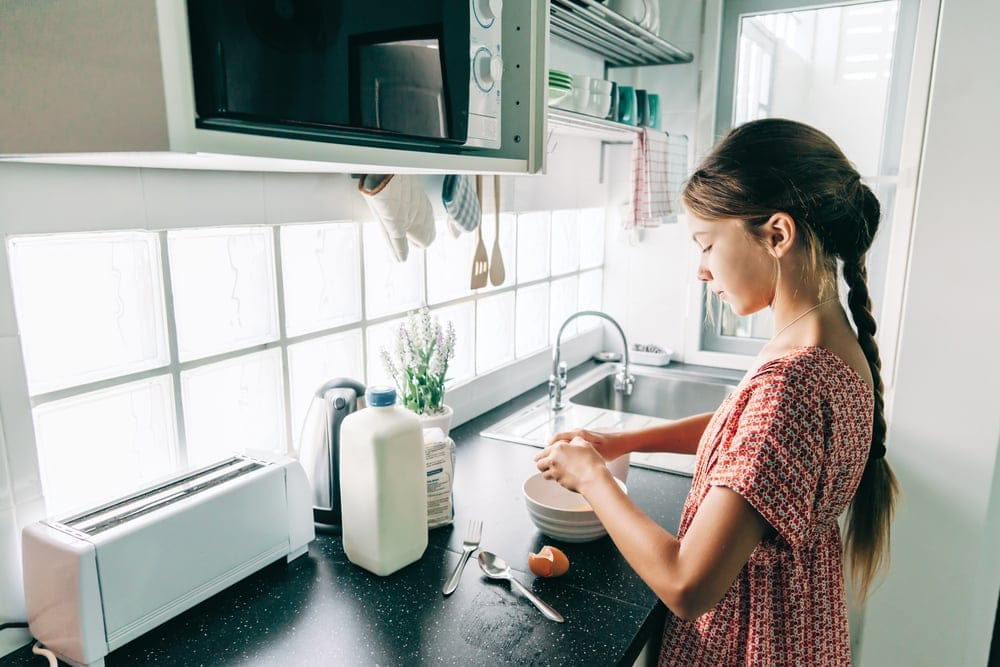A 10-year old girl doing dishes alone in the kitchen