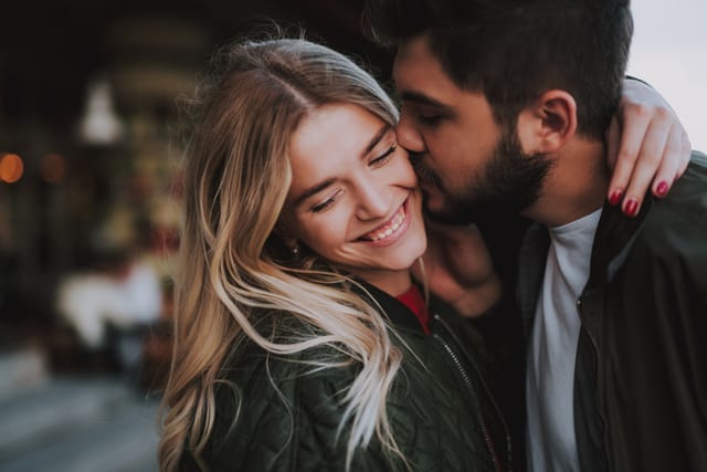man kissing laughing woman's cheek