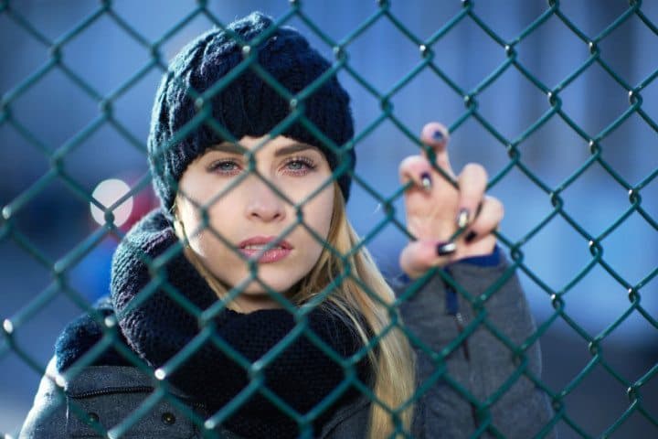Blonde in hat behind fence